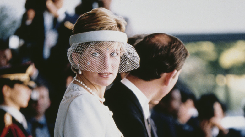 Princess Diana stands in hat 