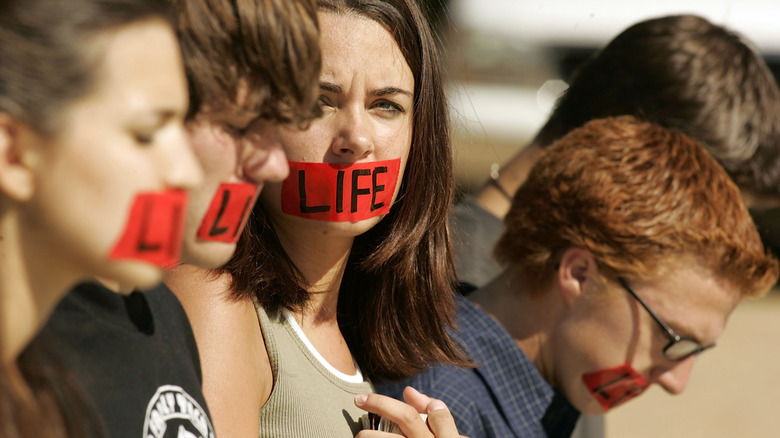 anti-abortion protestors with red duck tape across their mouths and the word "life" written across the tape