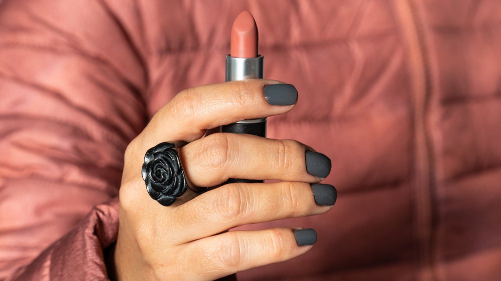 Hand holding up a nude color MAC lipstick