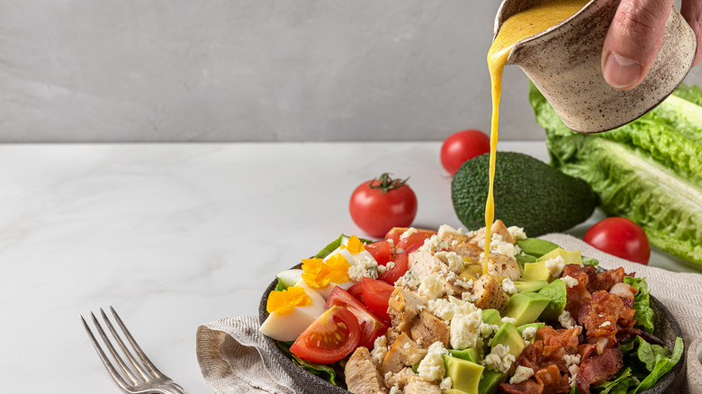 Hand pouring dressing on Cobb salad