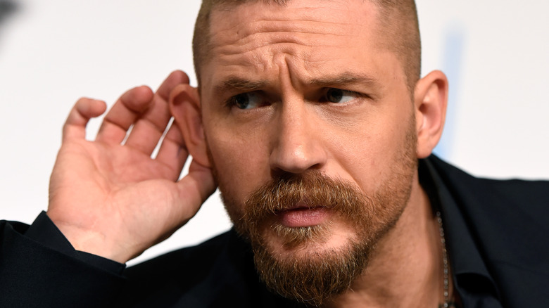 Tom Hardy holds his ear during an onstage interview