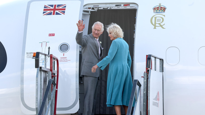 King Charles III waving as he boards a plane with Camilla, Queen Consort