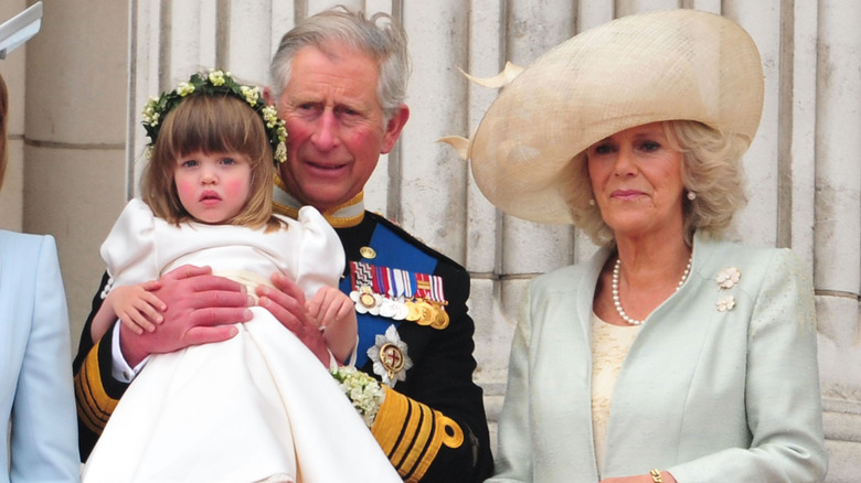 King Charles III on royal balcony holding three-year-old Eliza Lopes, standing next to Queen Camilla