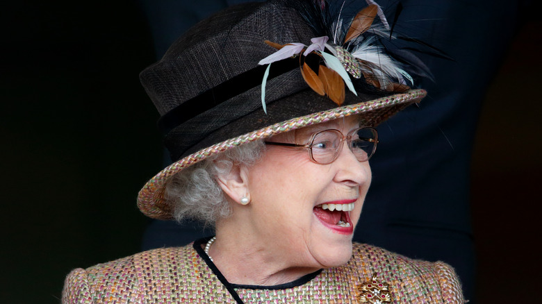 Queen Elizabeth II laughing while wearing a big hat