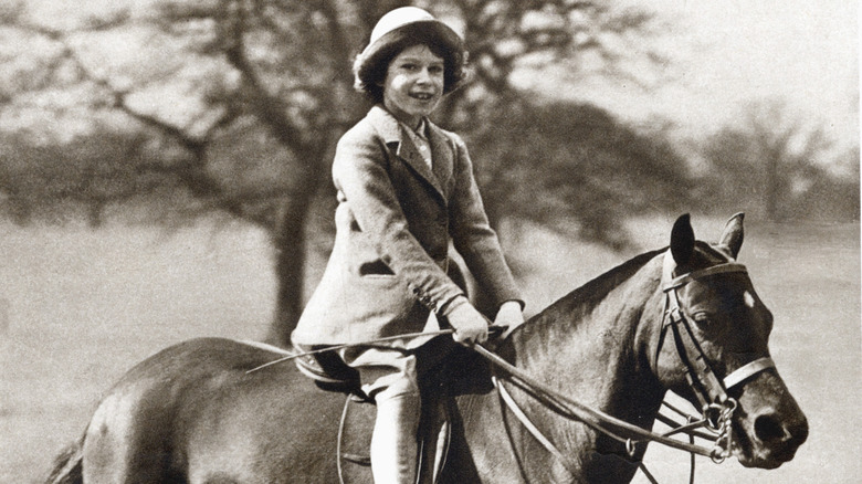 Queen Elizabeth smiling and riding a horse as a child