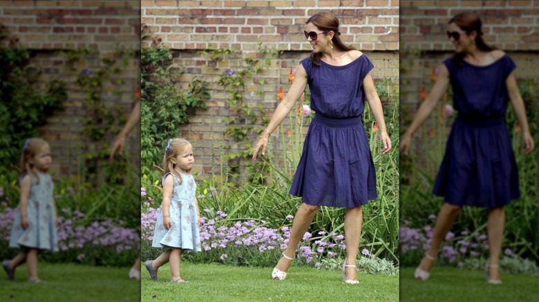 Princess Mary of Denmark holding her hand out to young Princess Josephine on lawn