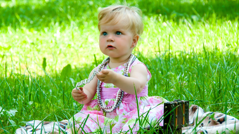 baby in dress wearing necklaces