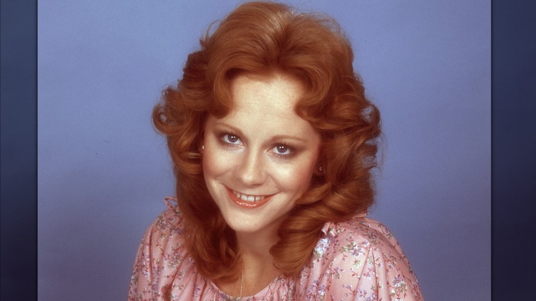 Reba McEntire in a posed portrait, smiling, with her hair in '70s era ringlets