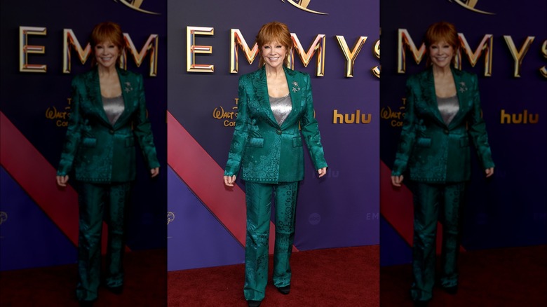 Reba McEntire smiling in a teal suit in front of a media wall.