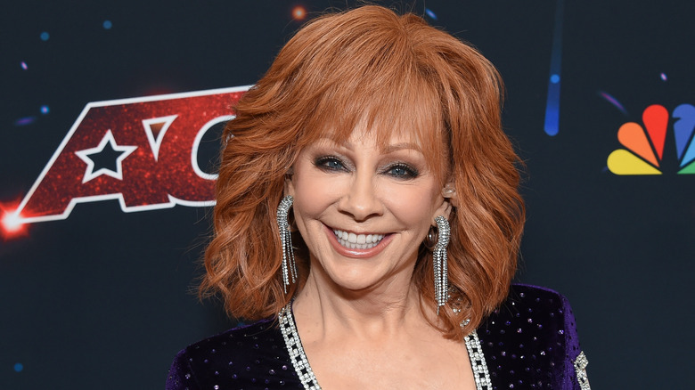 Reba McEntire smiling at camera, perfect makeup, dangling earrings.