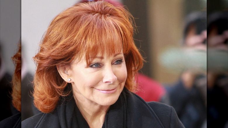 Reba McEntire outside, looking away but smiling, pale pink lipstick and eyeliner.