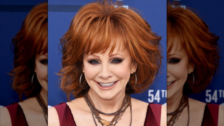 Reba McEntire smiling, very dark eye makeup, pale complexion.