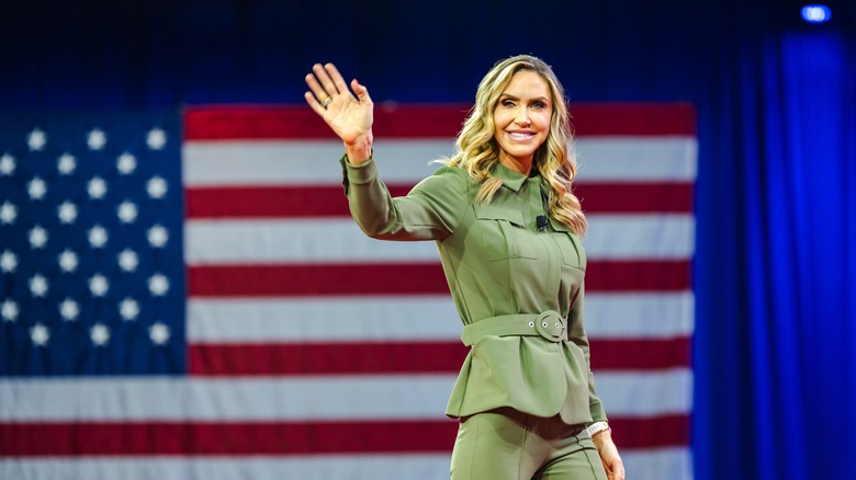 Lara Trump waves while standing in front of an American flag