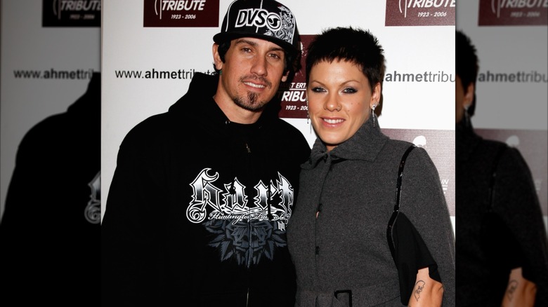 Carey Hart with black sweatshirt and ball cap and pink with short dark hair in a gray coat