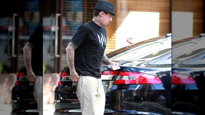 Carey Hart in black tee, hat, and khaki pants walking on street