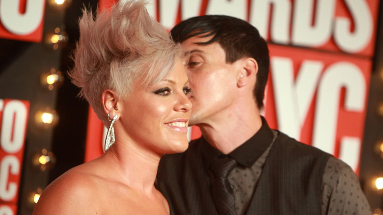 Pink with blonde faux hawk being kissed on cheek by Carey Hart in black dotted shirt with black vest and tie