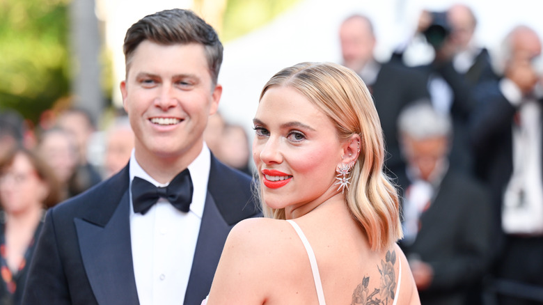 Scarlett Johansson looking over her shoulder with Colin Jost behind her in a tux