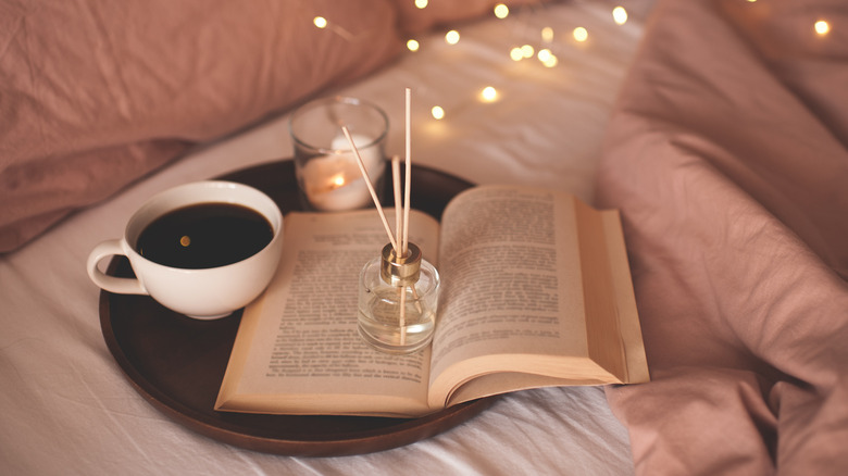 Reed diffuser, book, coffee, and candle on bed