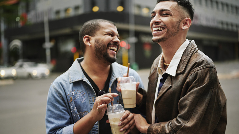 Gay couple holding coffees and laughing