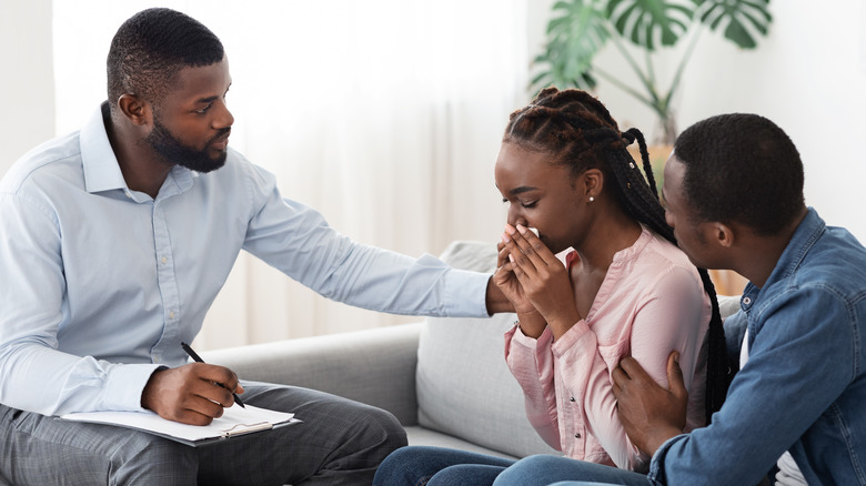 Woman crying while man and therapist comfort her