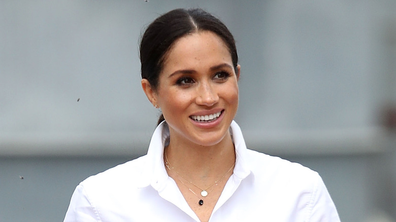 Meghan Markle walking and smiling in a white shirt