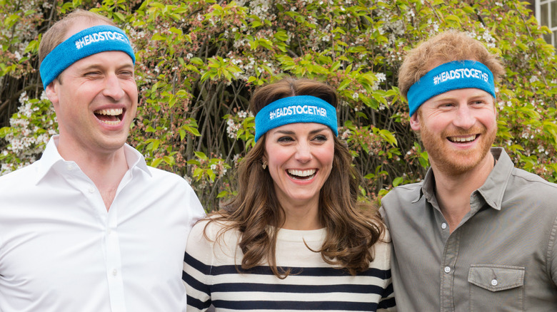 Prince William, Kate Middleton, and Prince Harry smiling and wearing blue headbands