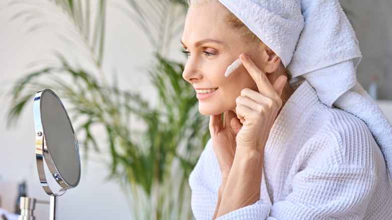 Woman applying moisturizer in mirror