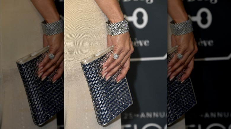 Jennifer Lopez's hand rocking a diamond pinky ring and a diamond bracelet while holding a clutch