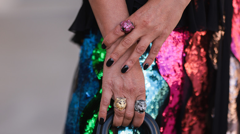 A woman with black nails shows off colorful statement rings on both hands