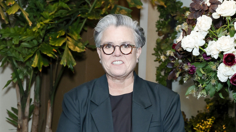 Rosie O'Donell standing near flowers in suit