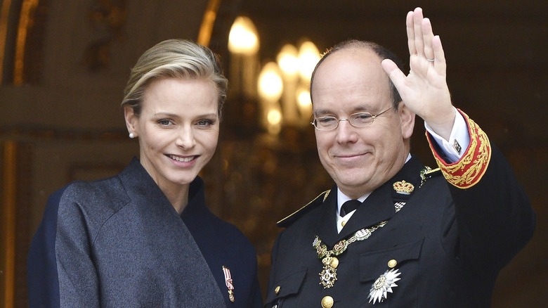 Princess Charlene smiling next to a waving Prince Albert II