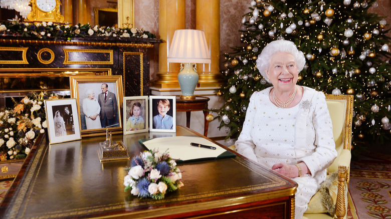 Queen Elizabeth II during holiday address seated at Christmas table with photos