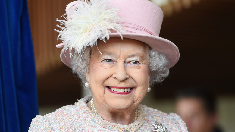 Queen Elizabeth smiling in a pink feathered hat