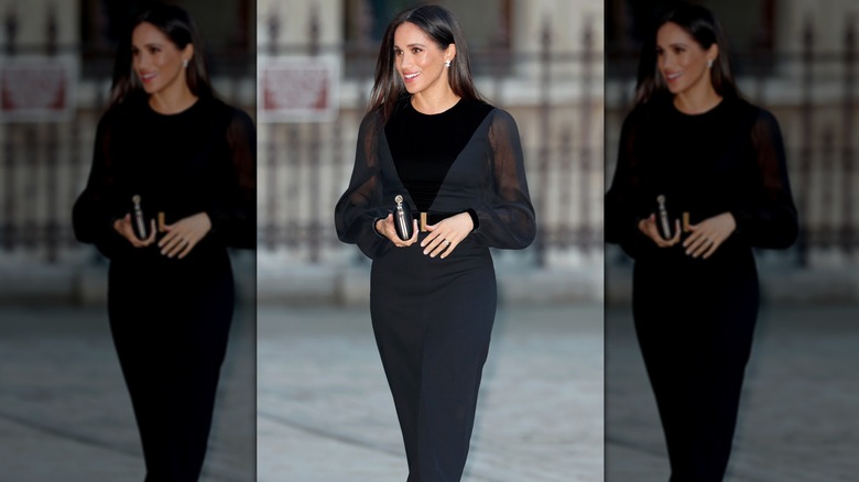 Meghan Markle smiling and walking in long black dress holding clutch bag