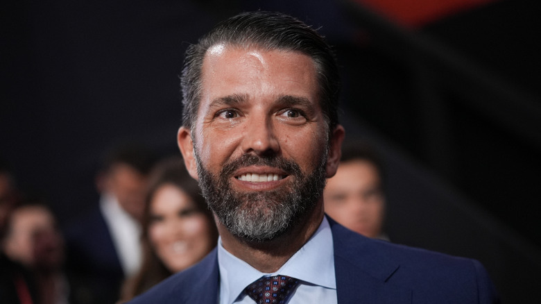 Donald Trump Jr. smiling in a navy suit