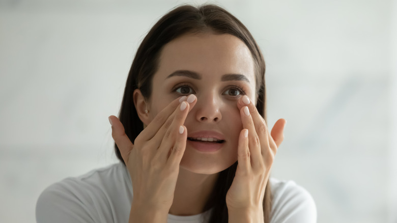 A woman dabbing her under eyes in a mirror 