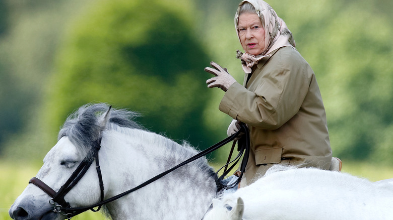 Queen Elizabeth riding her horse wearing a jacket and bonnet