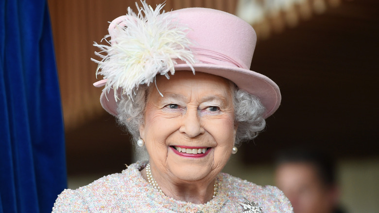 Queen Elizabeth wearing a pink hat with a feather in it