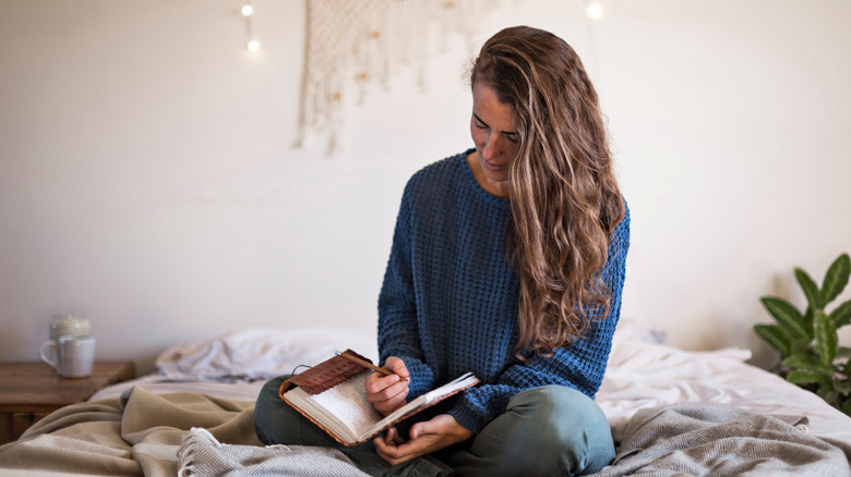 A woman writes in a journal while sitting in bed