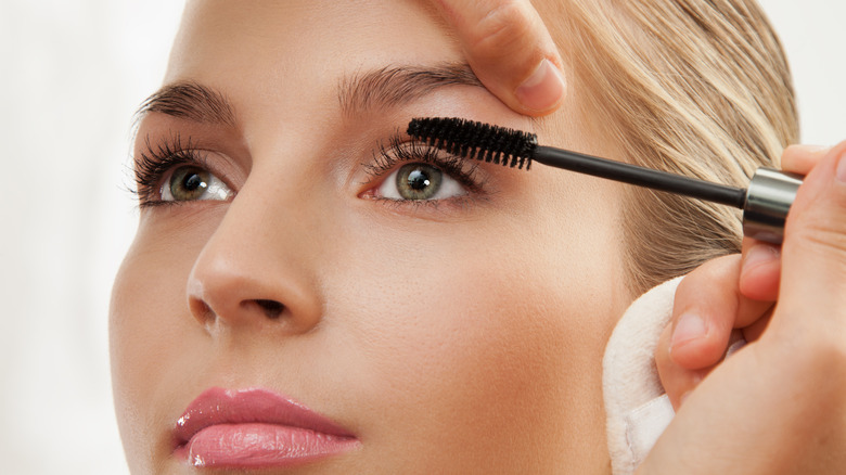 person applying curling mascara to woman with green eyes