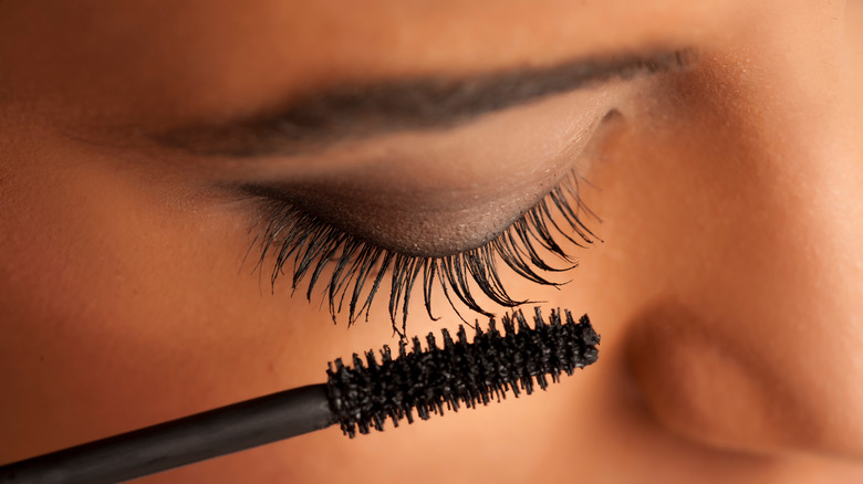 woman closing eyes and applying mascara