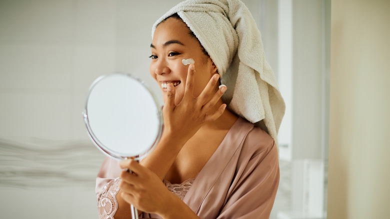 A woman applying face cream in a mirror 