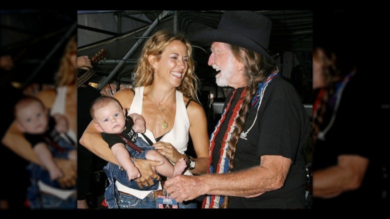 Sheryl Crow holding baby son and smiling with Willie Nelson