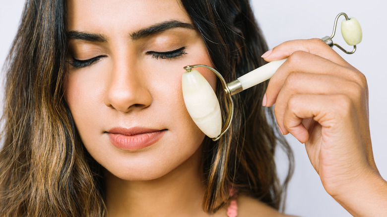 Young woman using a jade roller while wearing makeup