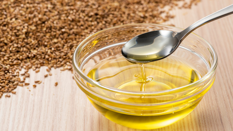 Flaxseed oil in a bowl with spoon surrounded by flaxseeds