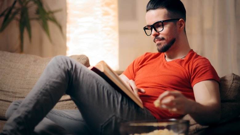 man eating popcorn and reading a book