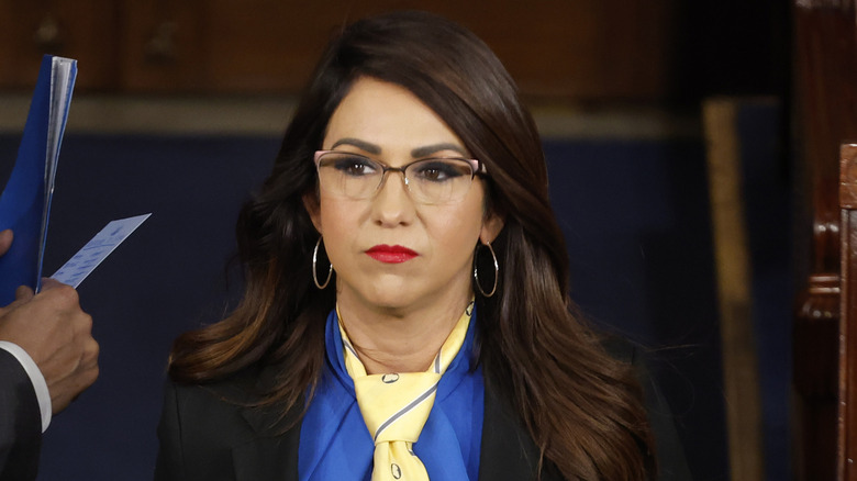 Lauren Boebert in glasses, hoop earrings, and red lipstick looking distressed