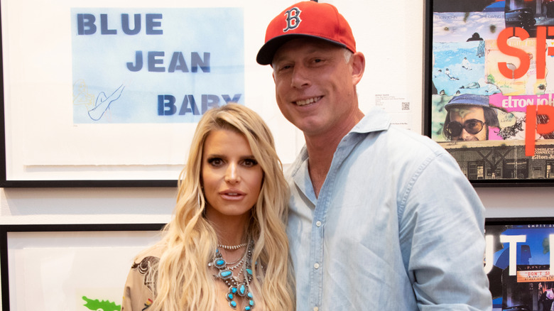 Eric Johnson wearing a red cap and putting a hand on Jessica Simpson's shoulder at Bernie Taupin's art exhibit