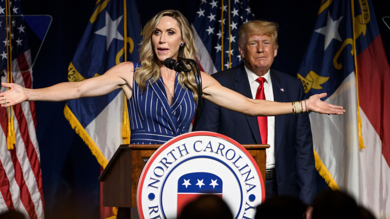 Lara Trump spreads her arms out while talking with Donald Trump standing in the background