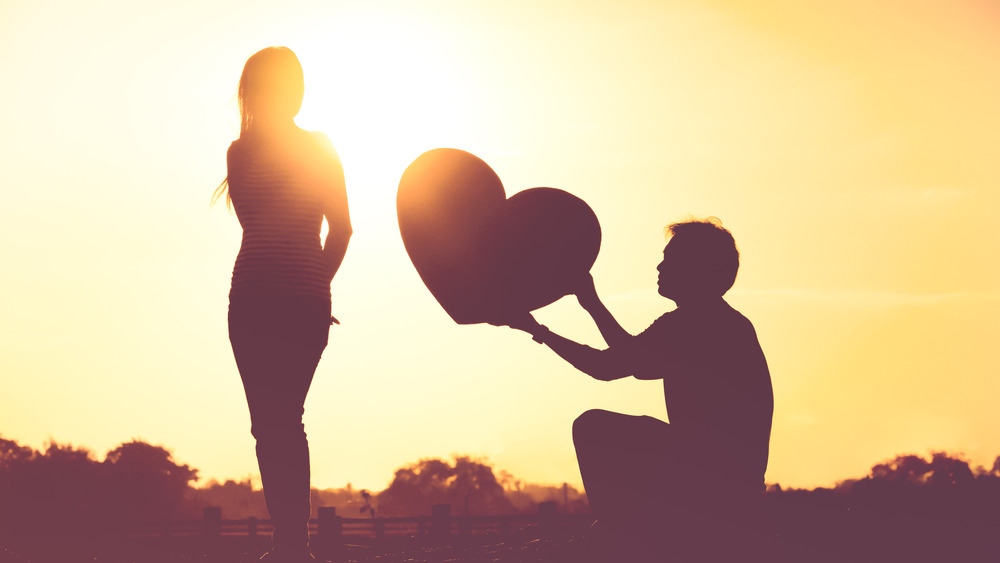 Man holding out cutout heart woman disinterested in silhouette